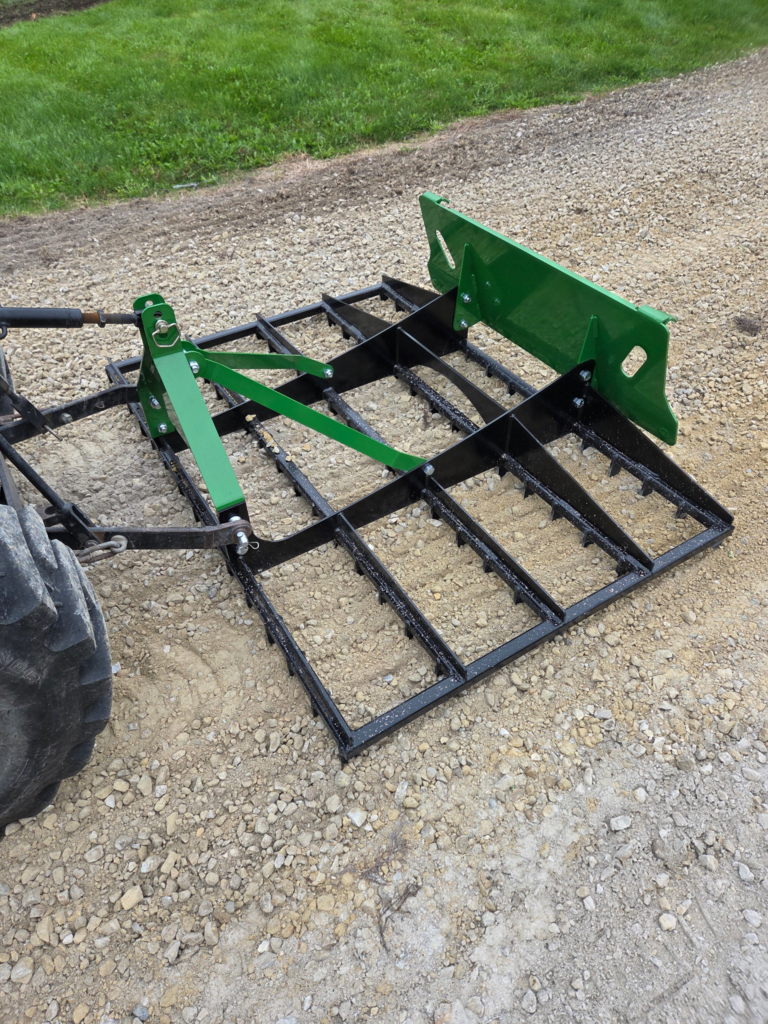 Operator view of the SWAT Metal Works 72" Compact Land Rake leveling and redistributing gravel behind a compact tractor.