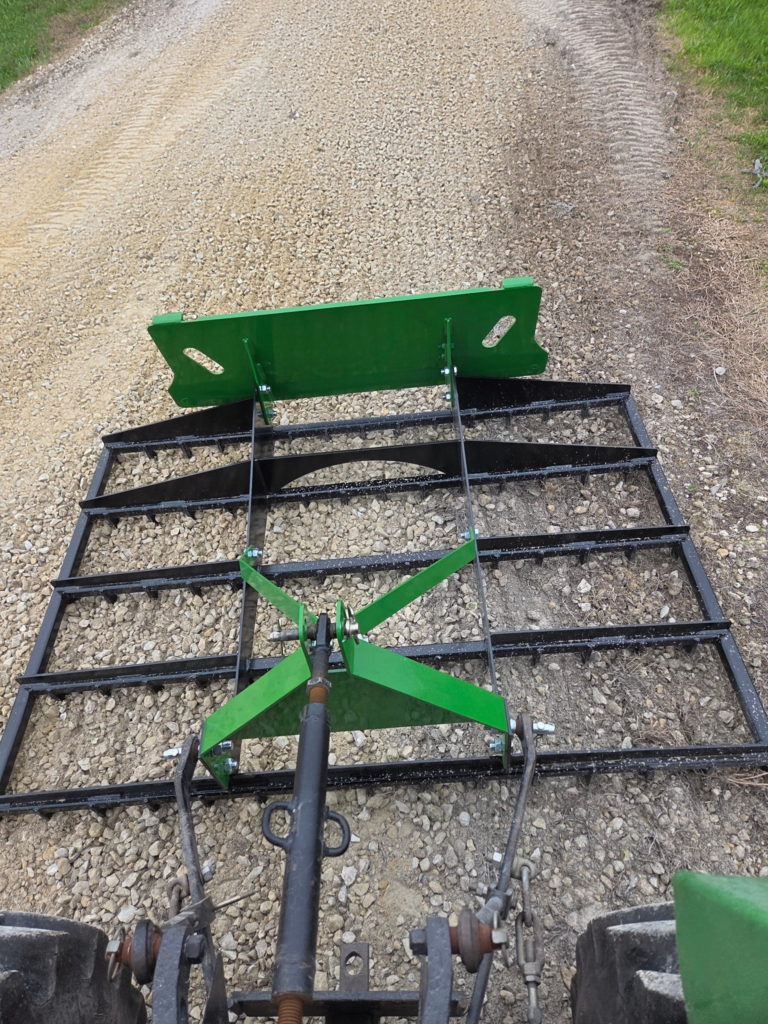 SWAT Metal Works 72" Compact Land Rake pulled behind a compact tractor for gravel driveway grading.