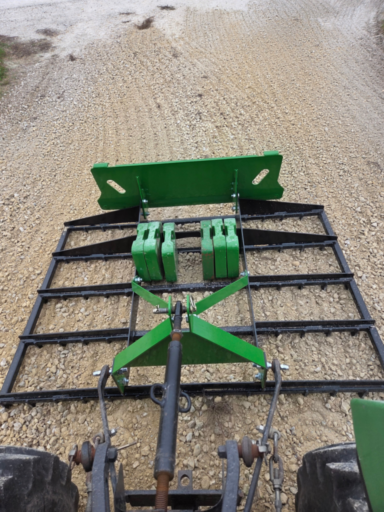 SWAT Metal Works 72" Compact Land Rake shown behind a compact tractor while grading gravel with added ballast on the rake.