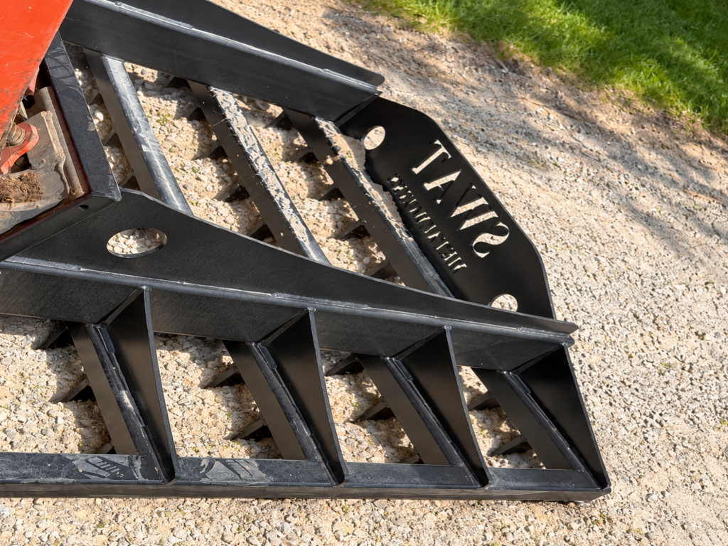 Low close-up of the SWAT Metal Works Skid Steer Land Rake showing the heavy-duty scarifier teeth and reinforced frame