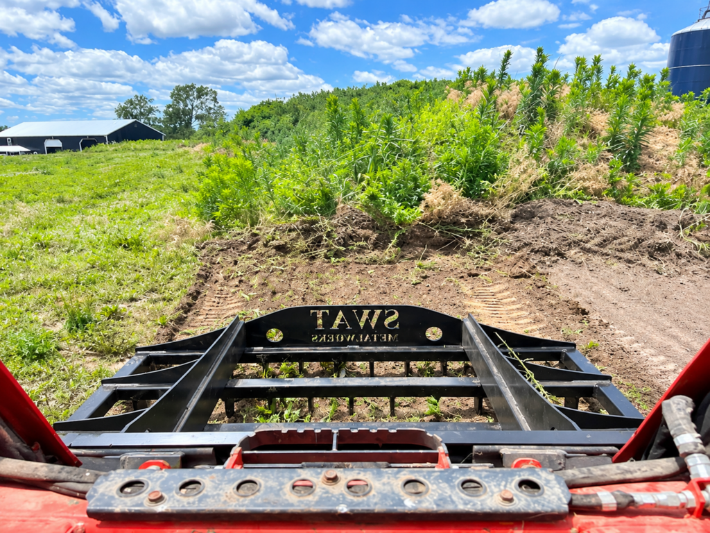 Operator view of a SWAT Metal Works Skid Steer Land Rake conditioning rough ground