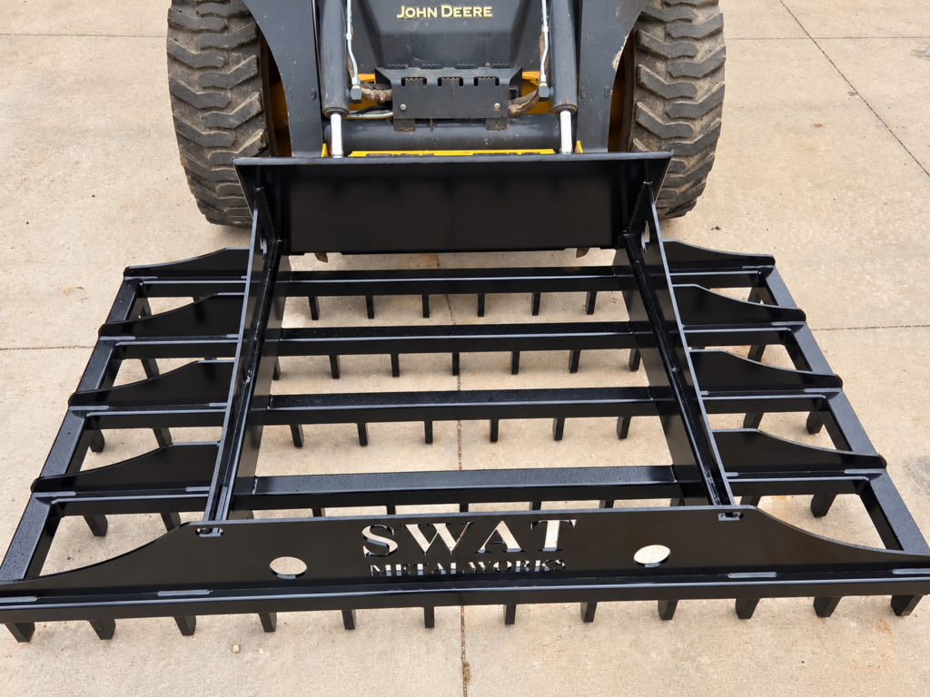 Wide front view of the SWAT Metal Works Skid Steer Land Rake mounted to a John Deere skid steer