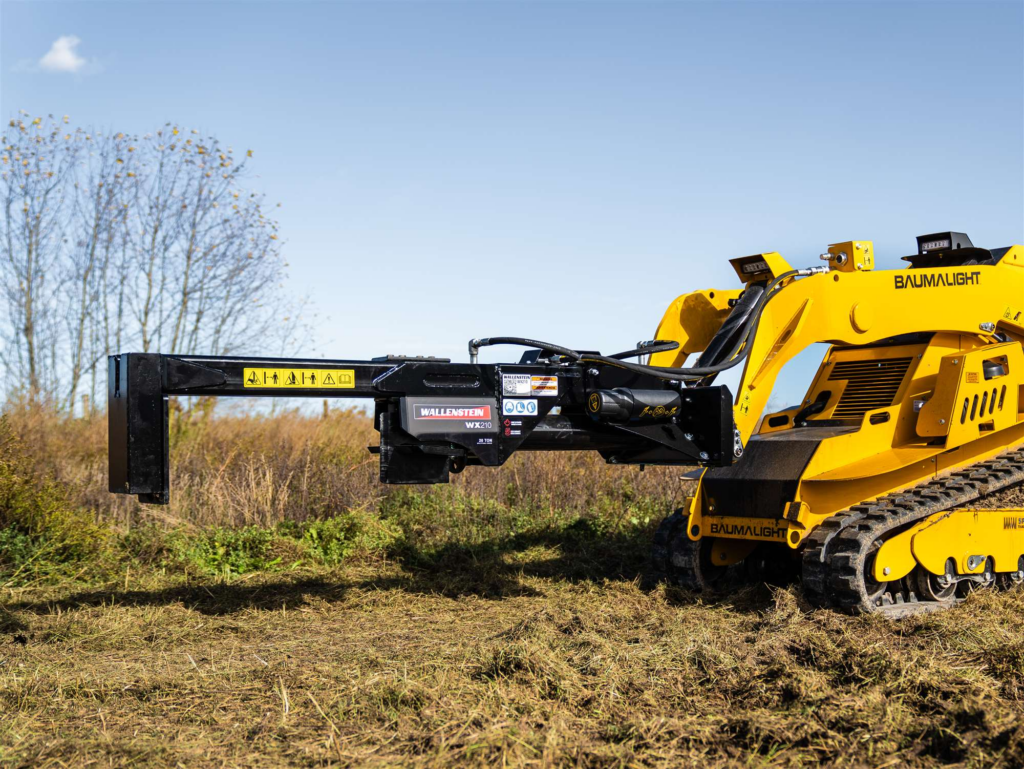 Side view of the Wallenstein WX210 mini skid steer log splitter mounted on a compact track loader in a field.